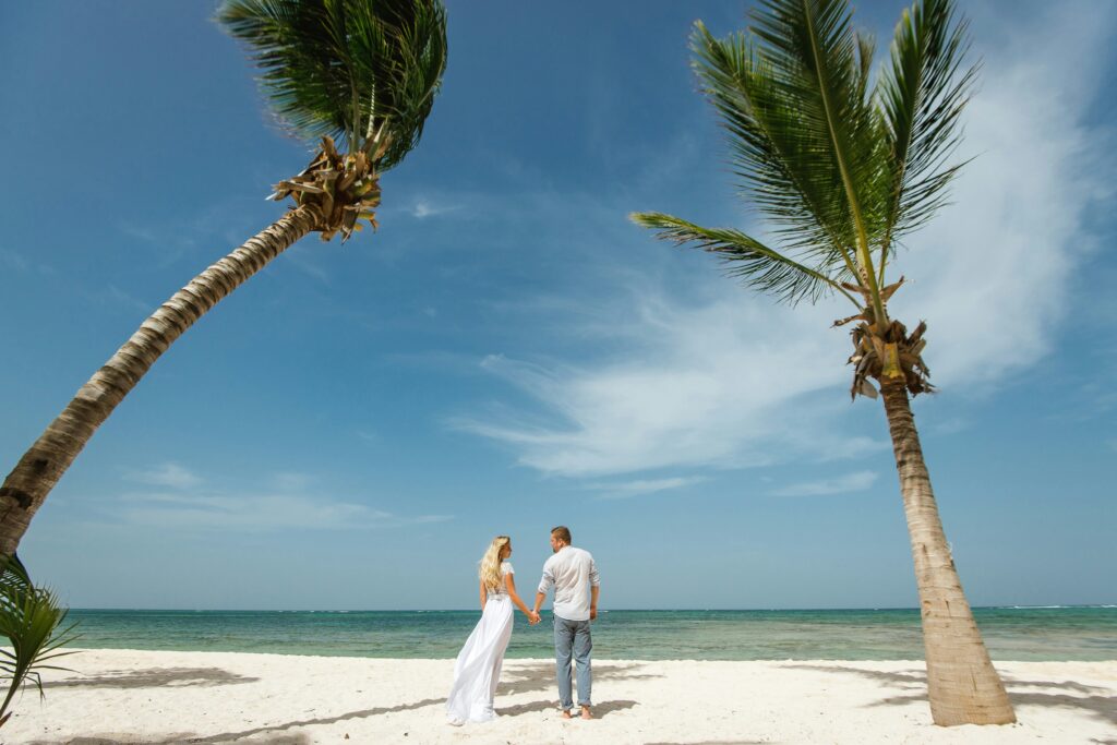 A couple on a beach holding hands under a couple of palm trees