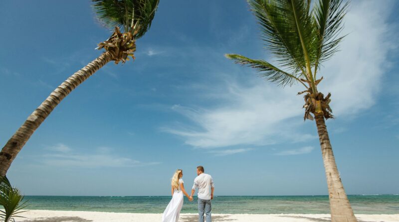 A couple on a beach holding hands under a couple of palm trees