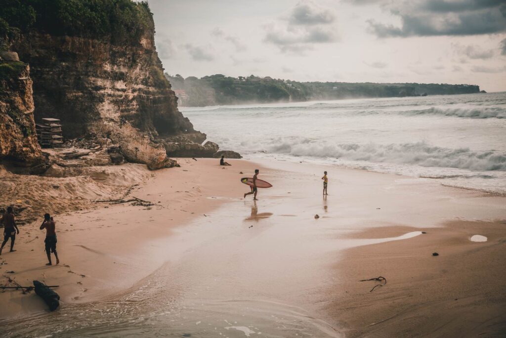 Bali vs Thailand beaches — surfers at Uluwatu cliff beach Bali Indonesia